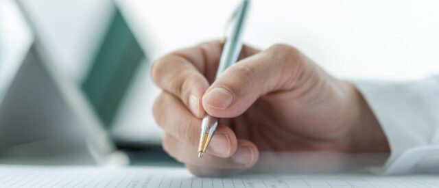 An individual is using a pen to write on a sheet of paper, demonstrating concentration.